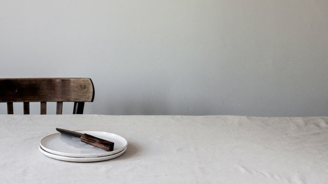 Tablesetting with a hand-thrown ceramic plate, a handcrafted knife and a wooden chair 