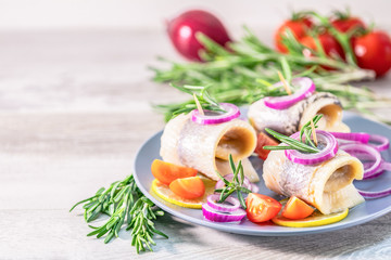 Delicious rolled herring fillet with red onion, cherry tomatoes, lemon and rosemary