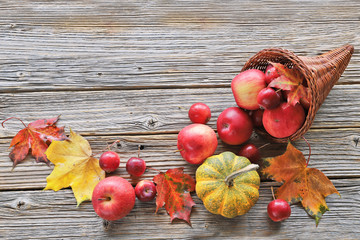 Cornucopia with apples, autumn leaves, pumpkins on wooden background 