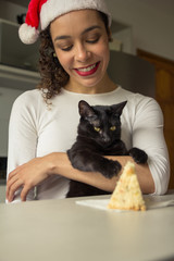 Woman wearing christmas hat and domestic cat with panettone at home.
