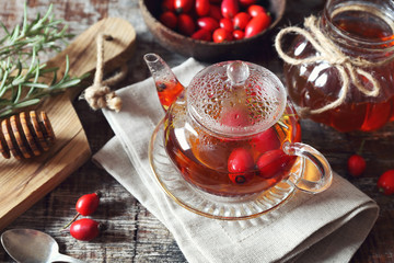 Healthy beverage. Rose hip tea in teapot, rosemary, honey and berries