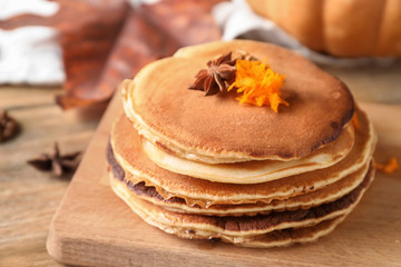 Stack of hot tasty pancakes with pumpkin on wooden board