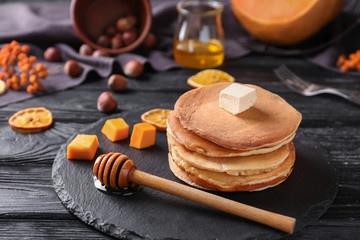 Stack of hot tasty pancakes with butter and pumpkin pieces on slate plate