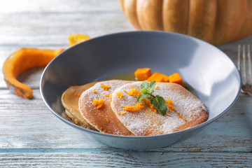 Hot tasty pancakes with pumpkin and honey in bowl on wooden table