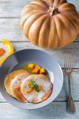 Hot tasty pancakes with pumpkin and honey in bowl on wooden table