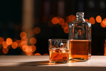 Glass and bottle of whiskey on wooden table against blurred lights