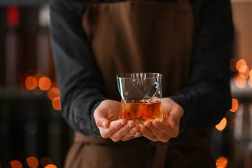 Female bartender holding glass of whiskey in bar, closeup