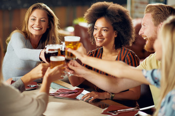 Friends making a toast while sitting in restaurant. Multi-ethnic group.
