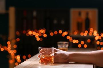 Man with glass of whiskey at wooden table in bar