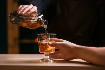 Female bartender pouring whiskey from bottle into glass in bar