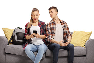 Teenage boy peeking at the phone of a teenage girl sitting next to him on a sofa