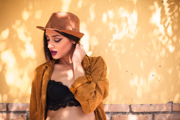 Attractive young woman with hat standing in front of yellow wall in the street
