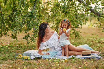 Happy family picking fresh organic fruits apples on farm. Smiling young family harvesting apples in summer garden. Harvest Concept.Greeting card for mother's day. Mother and daughter in apple orchard