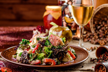vegetable salad with tomatoes, cheese and bell peppers on a brown plate and a glass of white wine on a dark wooden background. beautiful composition. Georgian cuisine. close-up