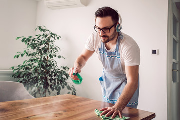 Young smiling man cleaning the table with a rag and spray bottle detergent