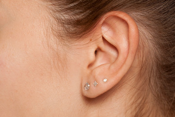 Closeup of female ear with three earrings - obrazy, fototapety, plakaty