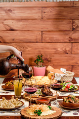 Georgian national cuisine. the girl pours red wine in a glass from an earthenware jug. table with Georgian dishes