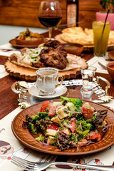 vegetable salad with tomatoes, cheese and bell peppers on a brown plate and a glass of white wine on a dark wooden background. beautiful composition. Georgian cuisine. close-up