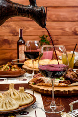 Georgian national cuisine. the girl pours red wine in a glass from an earthenware jug. table with Georgian dishes