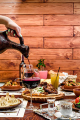Georgian national cuisine. the girl pours red wine in a glass from an earthenware jug. table with Georgian dishes