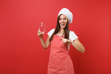 Housewife female chef cook or baker in striped apron white t-shirt toque chefs hat isolated on red wall background. Woman holding drinking clear fresh pure water from glass. Mock up copy space concept