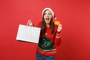 Excited Santa girl keeping mouth wide open, holding credit card, packages bags with purchases after...