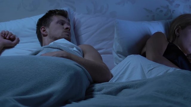 Upset woman and man lying apart on bed, crisis in relationship, misunderstanding