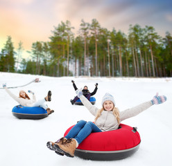 winter, leisure and entertainment concept - group of happy friends sliding down hill on snow tubes over natural background