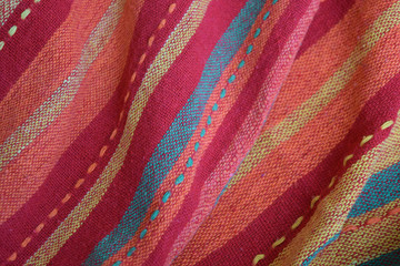 Fototapeta na wymiar Bright red-pink fabric with orange, khaki and pale yellow stripes arranged in folds. Top view background texture. Close up. Copy space.