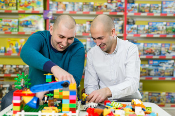 .Two adult men with happy faces create colorful constructions of toy bricks. Two adult men build of plastic blocks.
