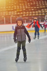 Adorable little boy in winter clothes with protections skating on ice rink
