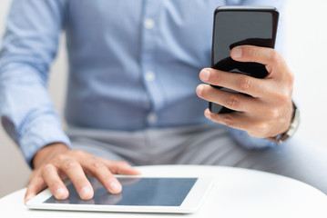 Closeup of man using smartphone and tablet computer. Business man using digital devices. Technology and communication concept. Cropped front view.