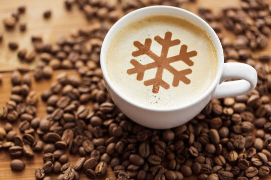 winter holidays and hot drinks concept - close up coffee cup with snowflake stencil picture and roasted beans on wooden table