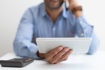 Closeup of man working, using calculator and tablet. Business man calling on phone. Technologies in business concept. Cropped front view.