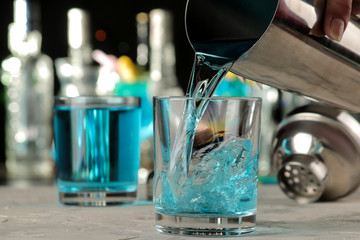 barman pours a blue lagoon cocktail from a shaker into a glass at the bar. cocktail preparation.
