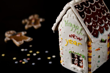 White gingerbread house with a brown roof, a window and the inscription happy New Year on a white wall
