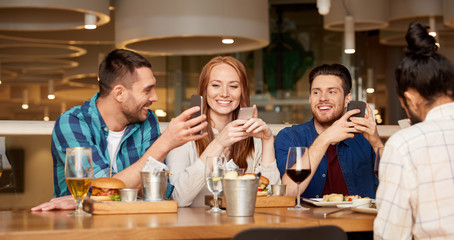 leisure, technology, lifestyle and people concept - happy friends with smartphones dining at restaurant