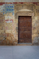 Fototapeta na wymiar Old wooden door framed by bricks stone wall at the courtyard of al Razzaz historic house, Darb al Ahmar district, Old Cairo, Egypt