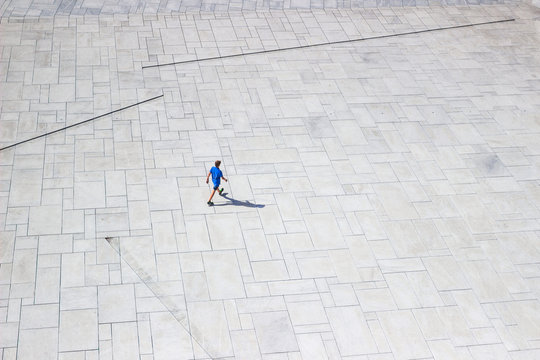 OSLO, NORWAY - AUG 10, 2016. Downright View At A Lonely Man Walking Like Ant On White Pavement Near Oslo Opera House. View From The Roof Of Opera In Sunny Summer Day. Isolated Man On White Background