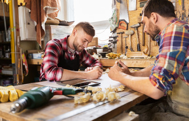 profession, technology and people concept - two carpenters with blueprint and tablet pc computer working at workshop