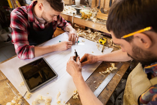 profession, technology and people concept - two carpenters with dividers or compass and ruler measuring blueprint at workshop