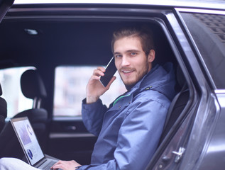 handsome businessman sitting in luxury limousine, working on laptop computer