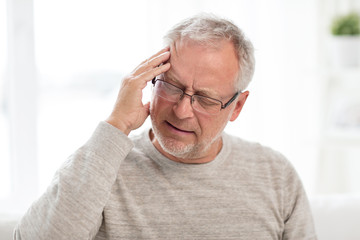 health care, stress, old age and people concept - senior man suffering from headache at home