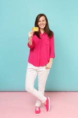 Full length portrait of smiling young woman in rose shirt blouse, white pants hold credit card...
