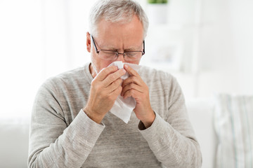 healthcare, flu, hygiene and people concept - sick senior man with paper wipe blowing his nose at...
