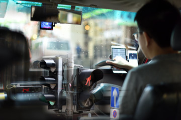 An energetic superimposed or double exposure of a Hong Kong taxi driver on his duty, looking from passenger back seats and a traffic light pole and street sign from a Hong Kong main street.