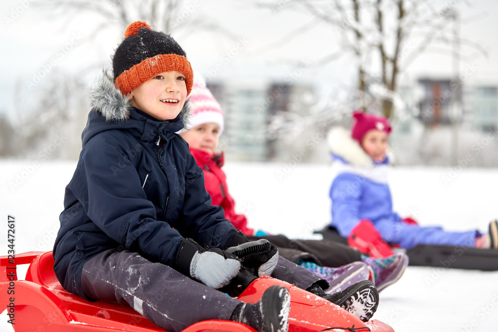 Poster childhood, sledging and season concept - group of happy little kids sliding on sleds in winter