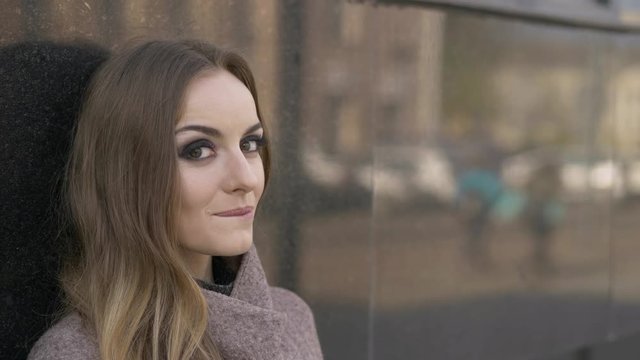 Beautiful fashionable blonde woman with gorgeous makeup in blush jacket slyly looking into camera move eyebrow. Close up slow motion portrait.