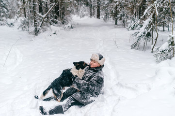 Fototapeta na wymiar Country woman in winter padded jacket covered ins now hugging her belowved funny dog. Eccentric unusual girl sitting in snow in wood and playing with frozen puppy. Adult lady with pet walk in forest.