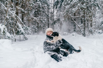 Fototapeta na wymiar Country woman in winter padded jacket covered ins now hugging her belowved funny dog. Eccentric unusual girl sitting in snow in wood and playing with frozen puppy. Adult lady with pet walk in forest.